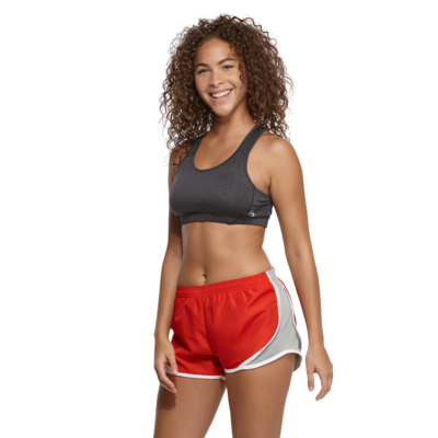young woman angled to the front in a dark grey sports bra and red and grey running shorts