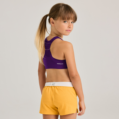 girl facing side wearing navy top and yellow shorts 1210G