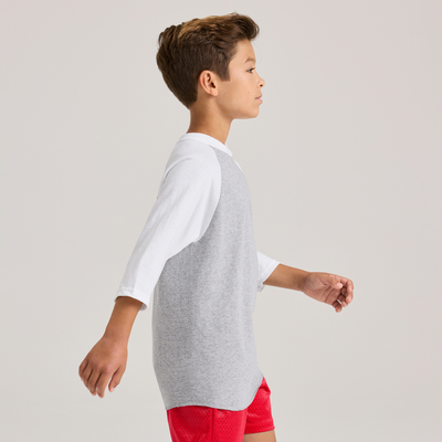 boy facing side wearing a grey and white baseball t shirt and red shorts 210B